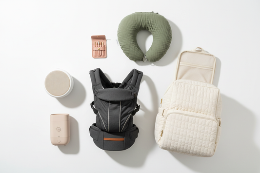 A flat lay of essential baby products including a  baby carrier, white noise machine, diaper bag backpack,  nail clipper set, bottle warmer, and nursing pillow  arranged on a white background.